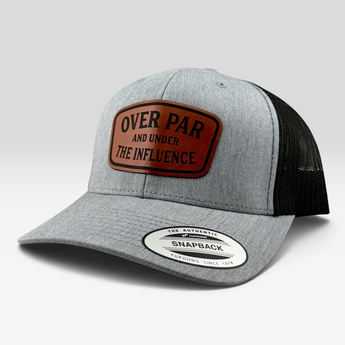 A heather gray and black trucker-style snapback cap with a brown leather patch on the front that reads 'OVER PAR AND UNDER THE INFLUENCE'.