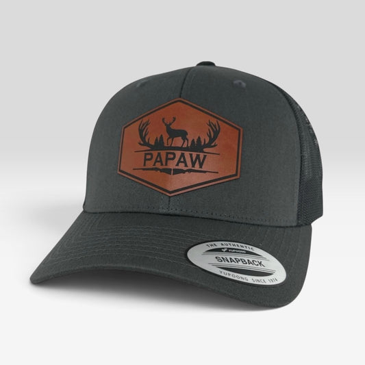A dark gray snapback trucker hat with a brown embroidered 'PAPAW' deer logo on the front, shown on a light gray background.