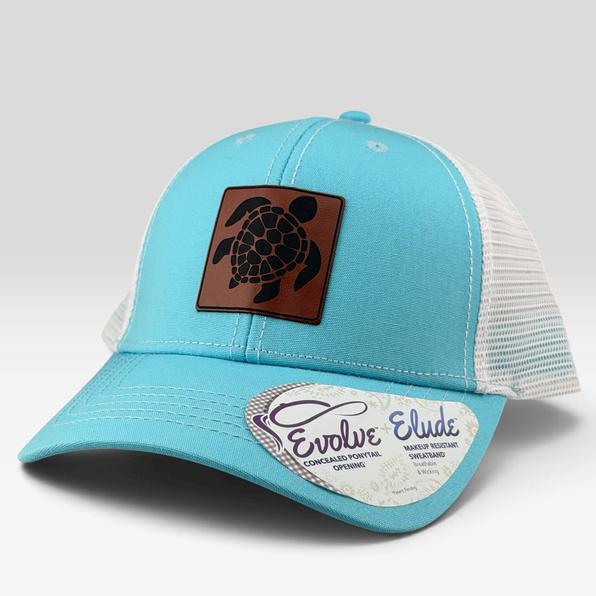 A light blue and white trucker hat with a brown leather patch featuring a black sea turtle design on the front. The brim has a white paper sticker that reads 'Evolve Elude'.