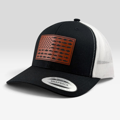 Black and white trucker hat with a brown leather patch on the front featuring a fish pattern resembling the American flag. The back of the cap is white mesh, and a silver Snapback sticker is visible on the brim.
